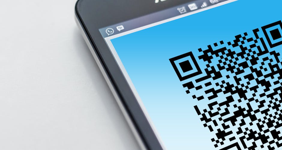 Person scanning a QR code on a smartphone with a laptop open in the background